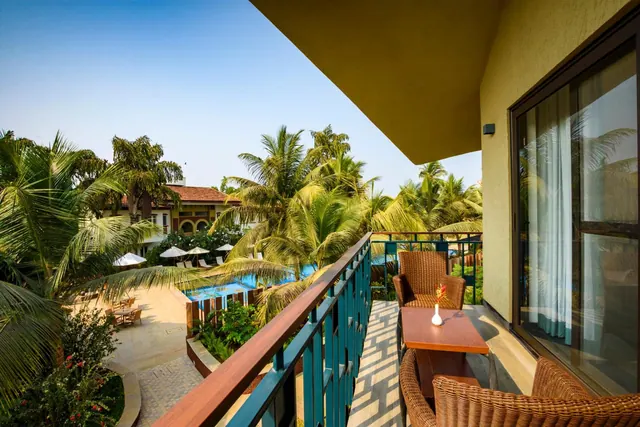 A furnished balcony overlooks a tropical garden and swimming pool.