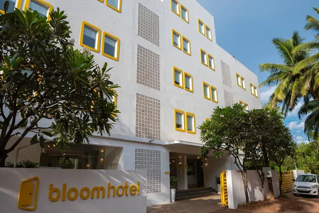 The Bloom Hotel facade is shown with yellow-trimmed windows, tropical trees, a hotel sign, and a parked car.