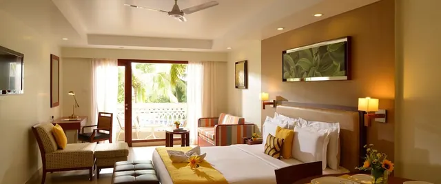 A spacious hotel bedroom opens onto a balcony overlooking palm trees.