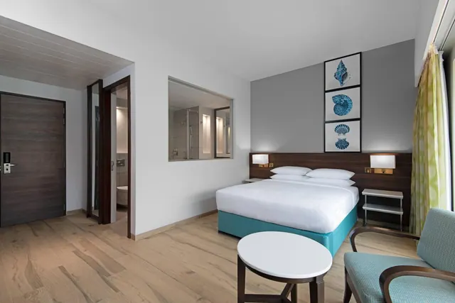 A bright modern bedroom has a double bed, seating area, wooden flooring and framed shell artwork.
