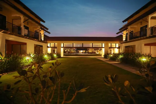 A lit hotel courtyard garden is framed by two-story buildings at dusk.