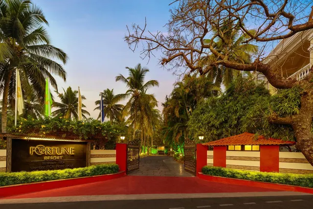 The resort entrance is framed by palm trees, landscaped greenery, flags and a tiled-roof gate structure.