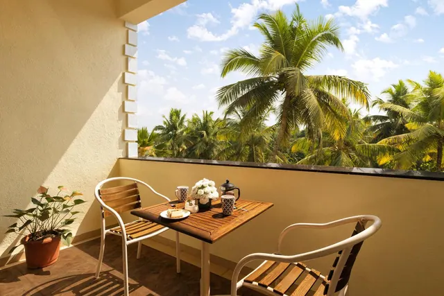 A furnished balcony with a table set for tea overlooks palm trees and tropical greenery.