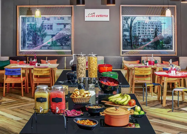 A bright dining room features a buffet spread, wooden tables and colorful chairs.