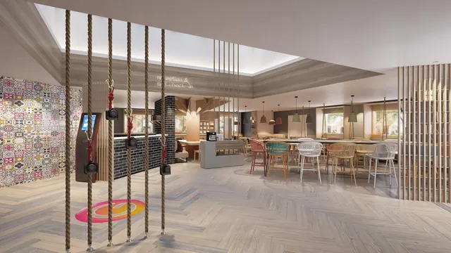 A bright hotel reception and lounge area has colorful chairs, pendant lights, and a decorative swing installation.