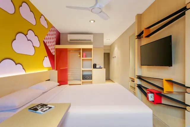 A bright modern bedroom with a double bed, colorful cloud wall decor, built-in storage, television, air conditioner and ceiling fan.