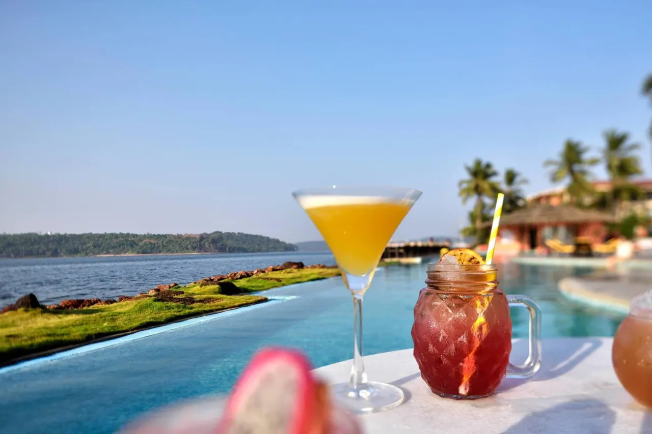 Drinks sit beside an infinity pool overlooking the sea and a tree-covered shoreline.