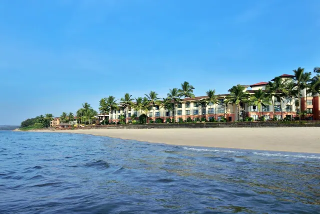 A palm-lined resort stands beside a sandy beach with the sea in the foreground.