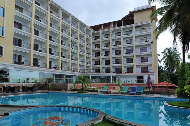 A large outdoor pool area with loungers and umbrellas is shown in front of a multi-storey hotel building.