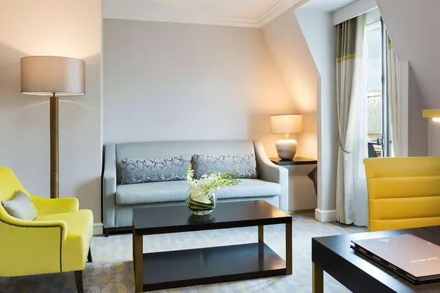 A bright sitting area contains a sofa, yellow armchairs, lamps, and a coffee table.