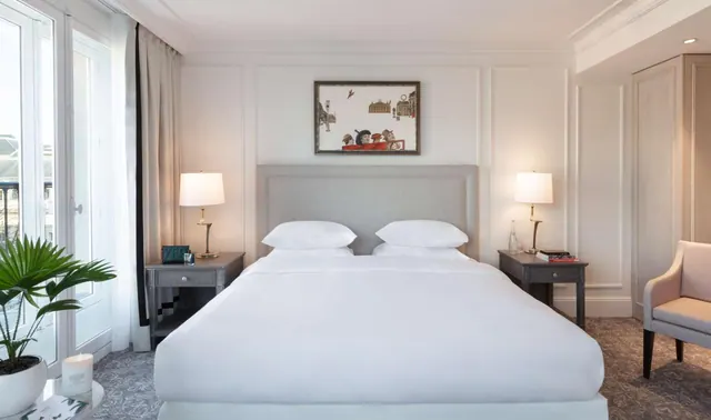 A bright bedroom with a large double bed, bedside tables, a chair, and doors opening onto a balcony.