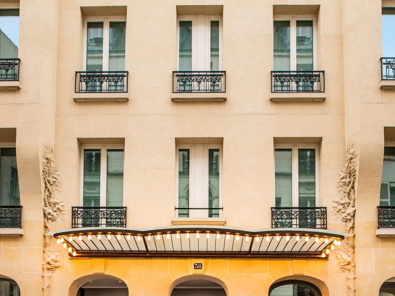 The hotel facade has ornate stone details, French windows, wrought-iron balconies and a lit entrance canopy.