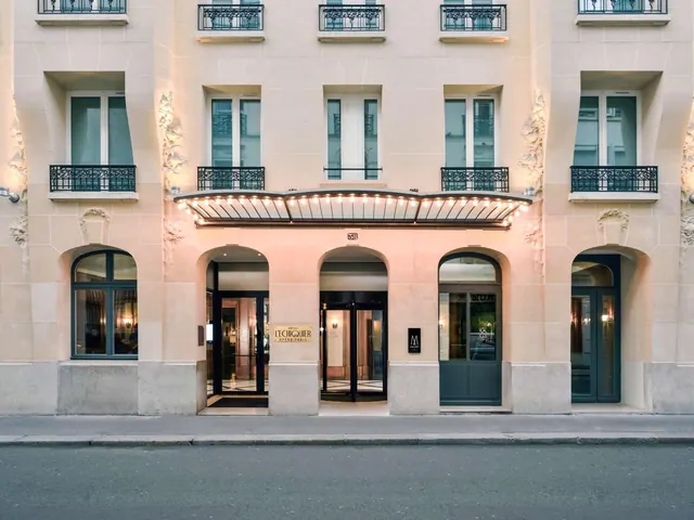 The hotel entrance is set in a classic Parisian building with ornate balconies and a lit canopy.
