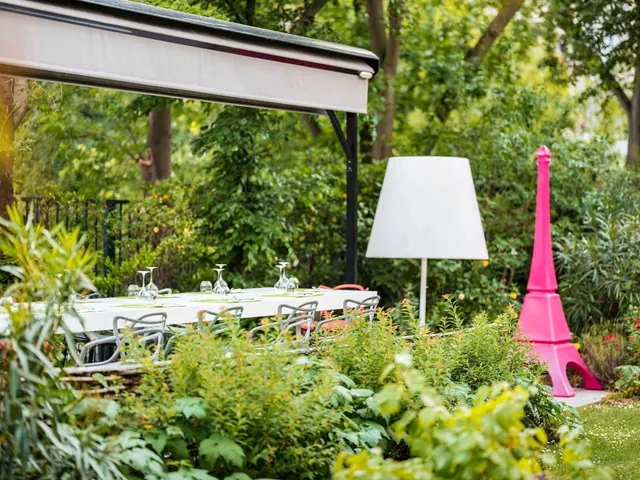 An outdoor dining table is set among garden greenery beneath a retractable canopy.