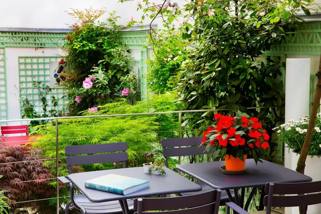 A furnished outdoor terrace is surrounded by flowering plants and a green trellis garden.