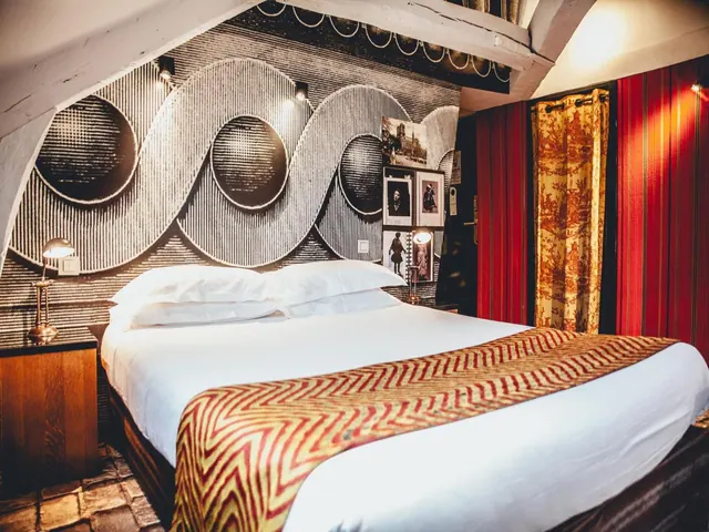 A double bed with white linens and a patterned runner stands against a bold black-and-white graphic wall in a decorated bedroom.