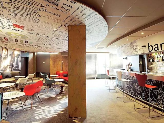 A bright hotel bar and lounge has colorful seating, round tables, and a long illustrated bar counter.
