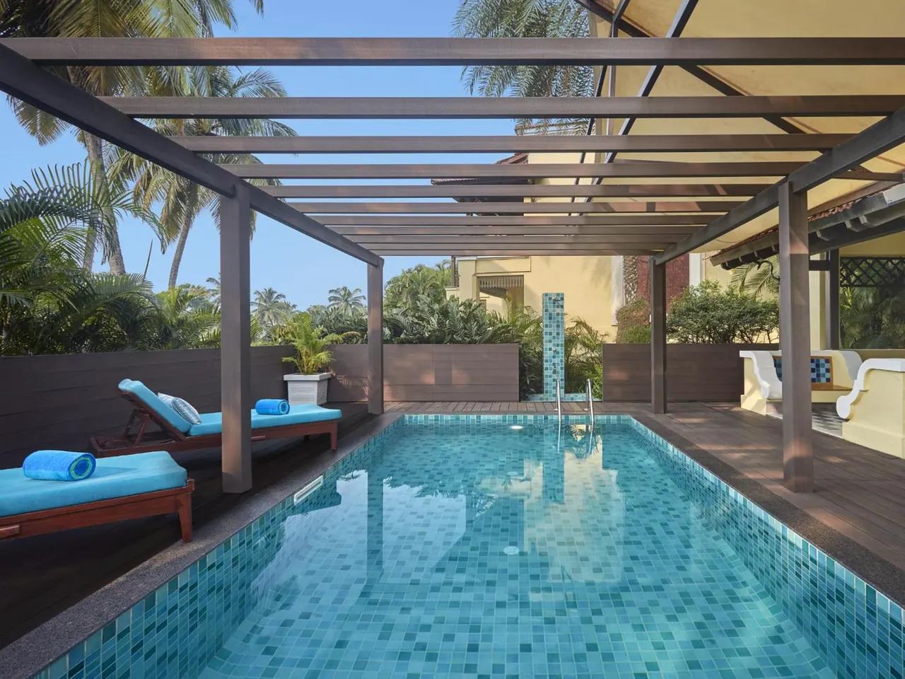 A private tiled pool with sun loungers sits beneath a shaded pergola amid tropical greenery.