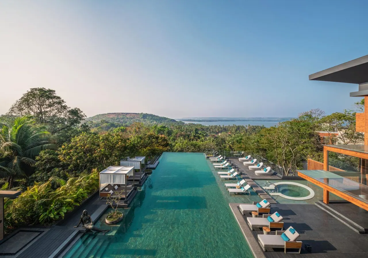A large infinity pool with loungers overlooks tropical greenery, hills and the sea.