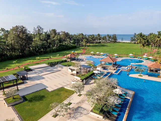 An expansive pool complex overlooks landscaped grounds, palm trees and the sea beyond.