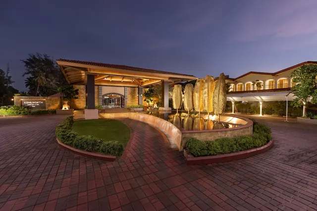 The hotel entrance is shown at dusk with a covered porte-cochère, landscaped grounds, and a decorative water feature.