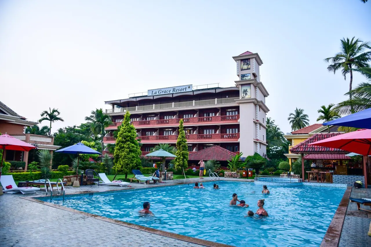 A large swimming pool with loungers and umbrellas sits in front of the La Grace Resort building.