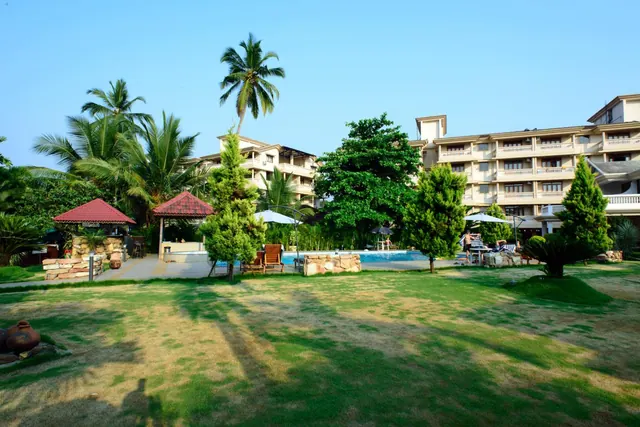 A landscaped tropical garden with a small pool, shaded seating, palm trees and the hotel buildings beyond.