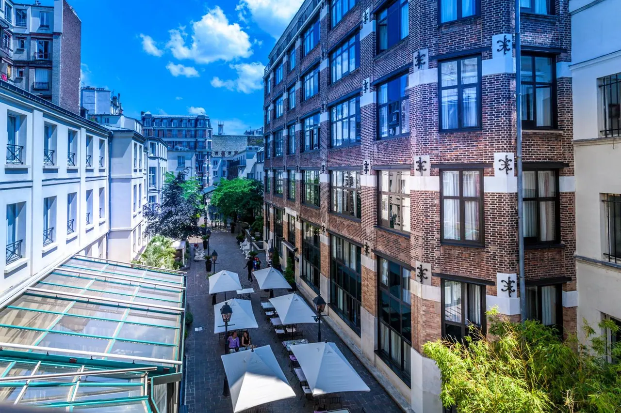 A view over a landscaped pedestrian courtyard with outdoor dining tables and surrounding Parisian buildings.