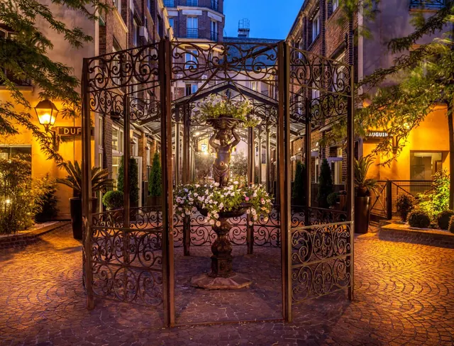 An ornate wrought-iron gate opens onto a landscaped hotel courtyard with a central statue and fountain.