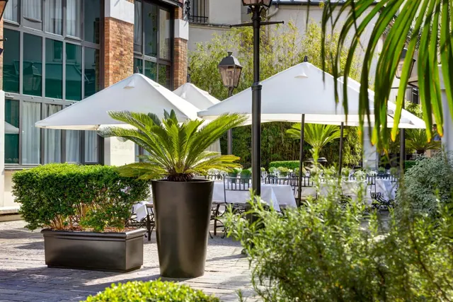 A landscaped courtyard has outdoor tables beneath white umbrellas beside the hotel building.