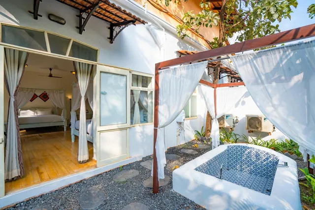 A canopied outdoor bathtub sits beside an open bedroom with a double bed and ceiling fan.