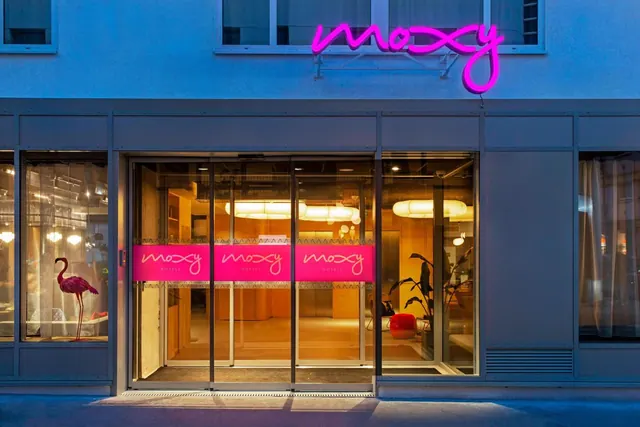 The Moxy hotel entrance is shown behind glass doors with illuminated signage and a flamingo display.