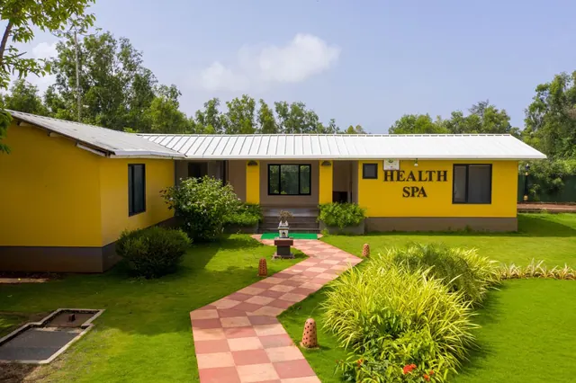 A yellow health spa building overlooks a manicured garden with a tiled walkway and ornamental plants.
