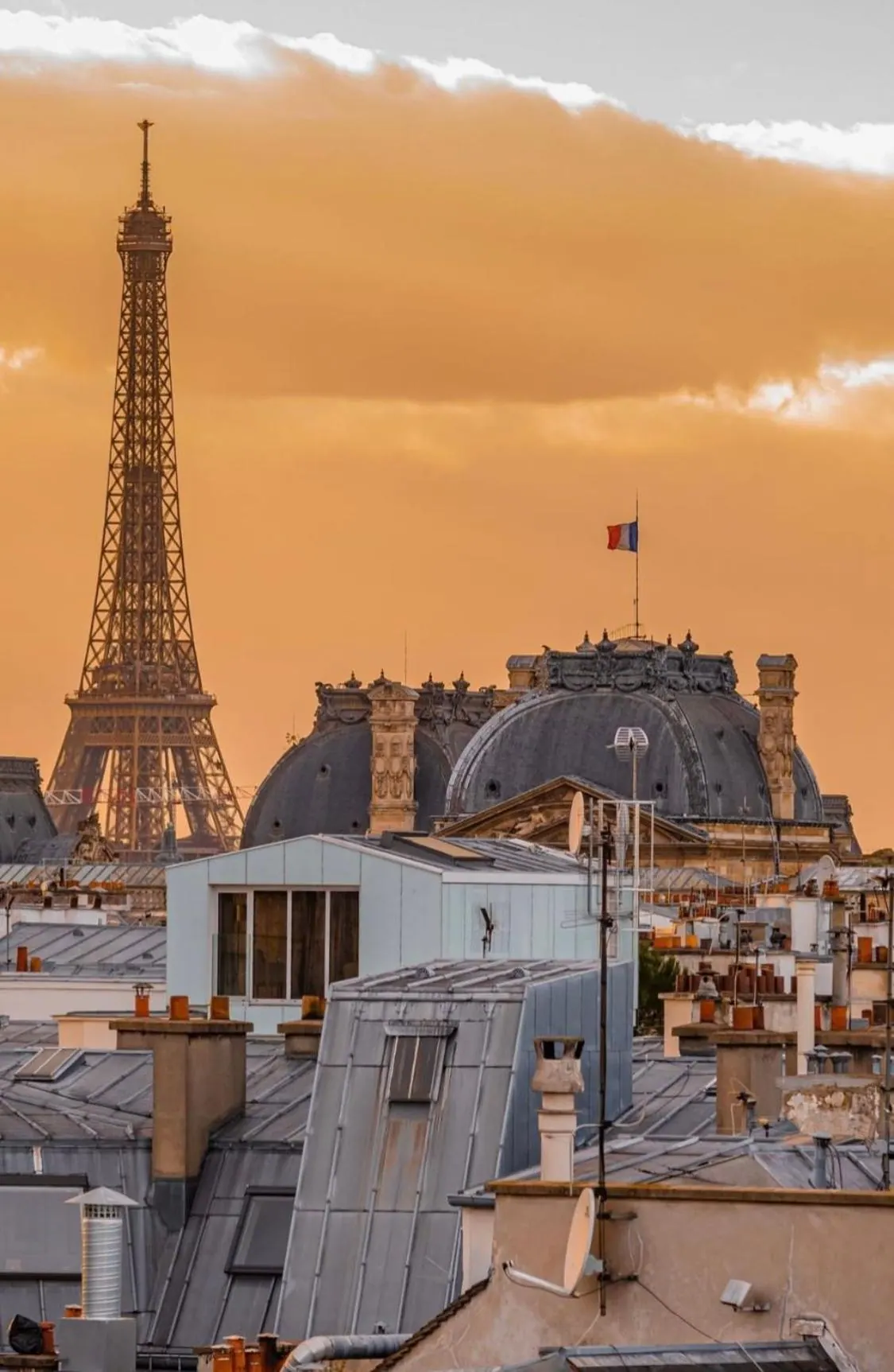 The Eiffel Tower rises above Parisian rooftops beside a domed historic building.