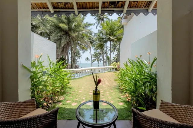 A covered terrace with wicker seating overlooks a tropical garden and the sea.