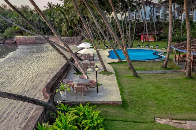 A sandy beach, palm-lined lawn, swimming pool and outdoor seating are visible within the property grounds.