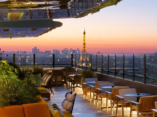A furnished rooftop terrace overlooks Paris and the illuminated Eiffel Tower at sunset.