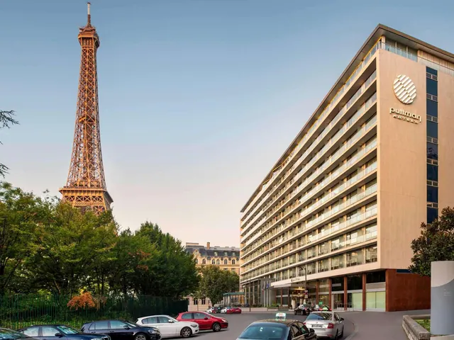 The Pullman hotel building stands beside the Eiffel Tower with trees and parked cars in the foreground.