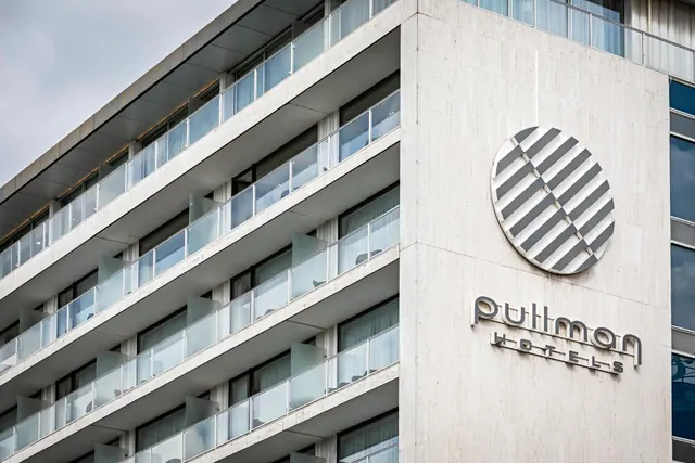 The modern hotel exterior has stacked glass-fronted balconies and the Pullman Hotels sign on a concrete facade.