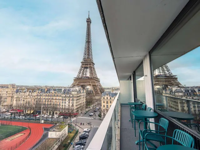 A furnished terrace overlooks the Eiffel Tower, Paris rooftops, and a nearby athletics track.