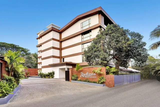 The Radisson Resort Goa Baga building is shown from the entrance driveway with landscaped planting around the sign.