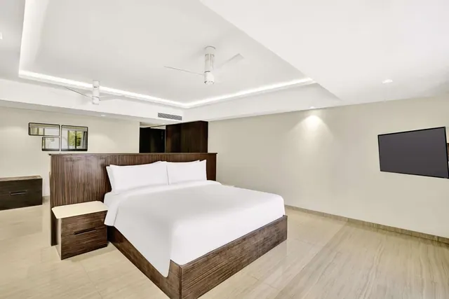 A bright modern bedroom with a double bed, wall-mounted television, ceiling fans and wood furnishings.