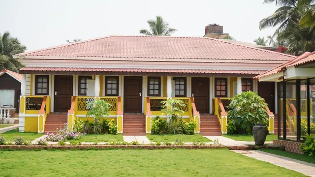 A colorful heritage-style building with covered entrances faces a landscaped lawn and palm trees.