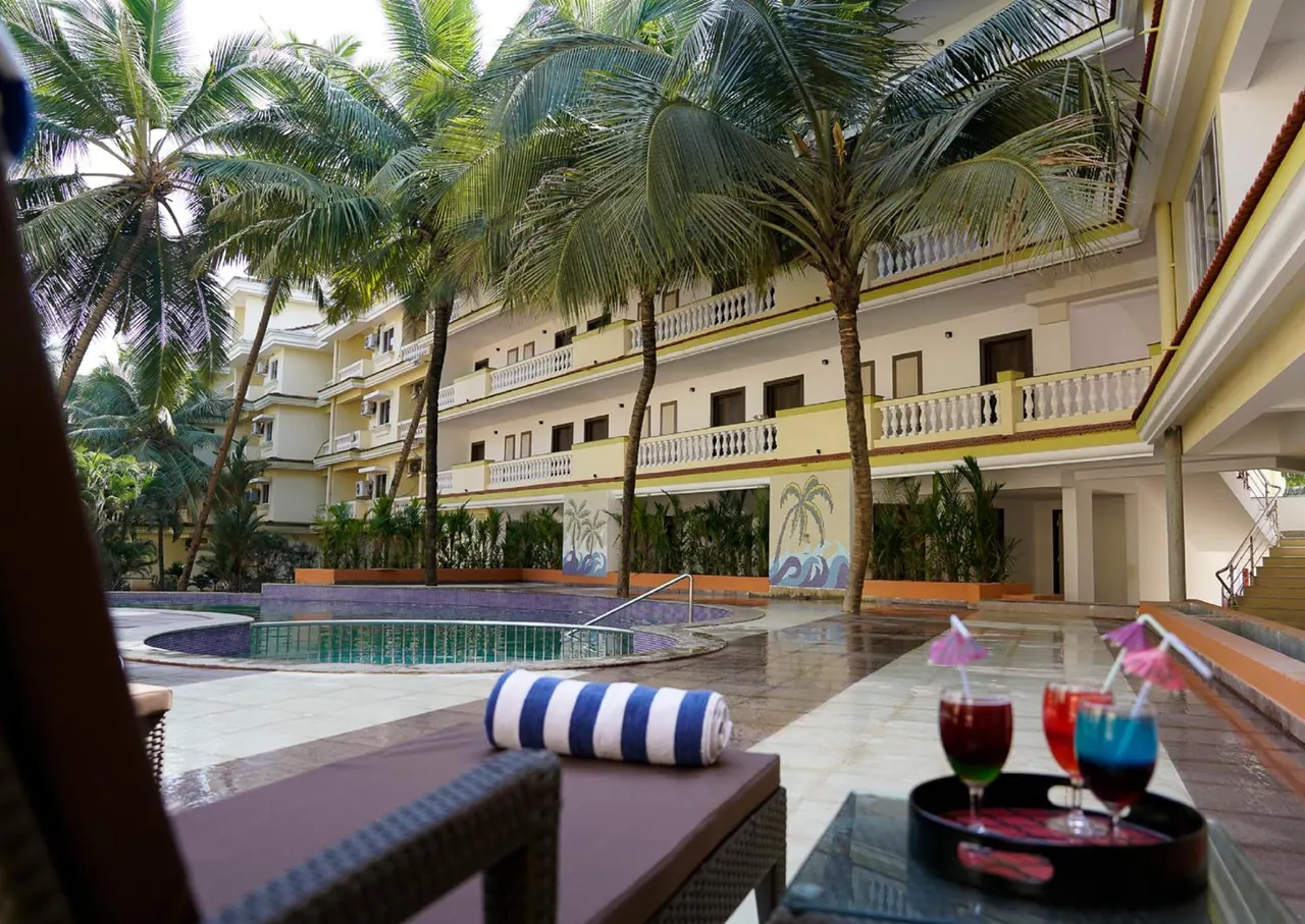 A courtyard pool is surrounded by palm trees, loungers, drinks and a multi-storey hotel building.