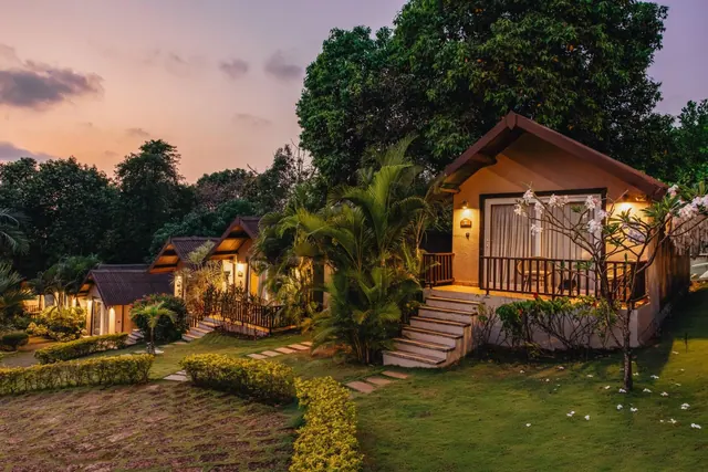 A row of illuminated tropical cottages sits among landscaped gardens at sunset.