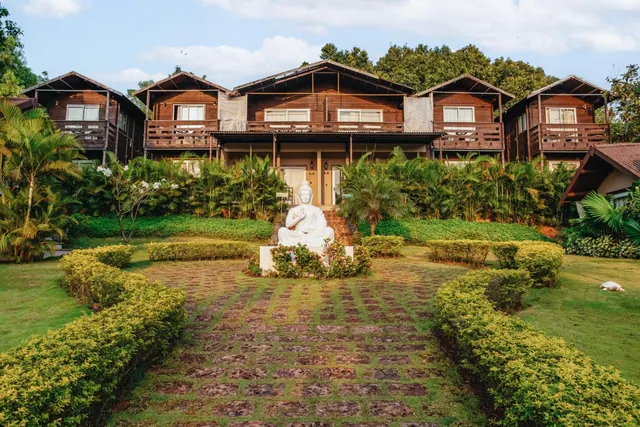 A wooden hotel building stands behind a landscaped garden with a central seated statue.