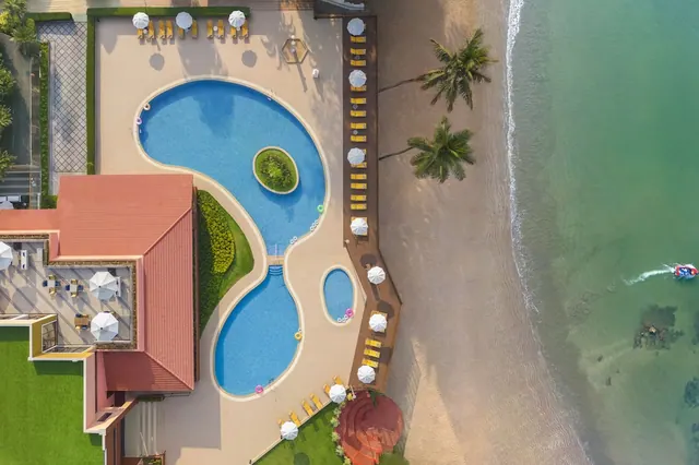 An aerial view shows several swimming pools, loungers and umbrellas beside a sandy beach and the sea.