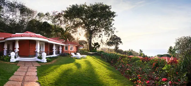 Red-roofed cottages border a landscaped lawn and flowering garden with the sea visible beyond.