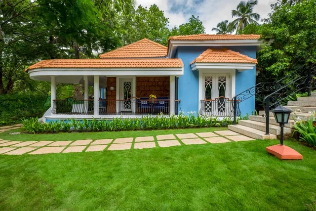 A blue heritage-style building with tiled roofs, covered verandas, and landscaped lawns is shown among tropical trees.