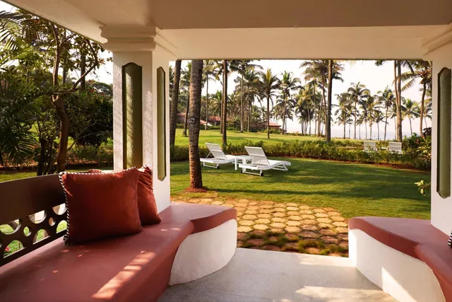 A covered terrace with built-in seating overlooks a palm-lined garden and the sea.
